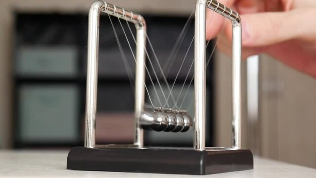 Close-up of Newton's cradle on the table and a man's fingers pulling back one ball and releasing it starting the pendulum
