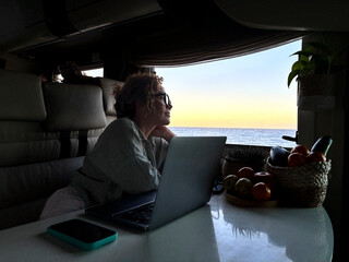 One modern adult woman digital nomad working on laptop sitting inside a motorhome camper van and...