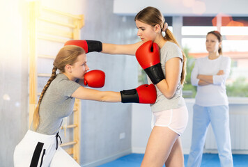 Focused teen girl wearing boxing gloves working out under guidance of female instructor during...
