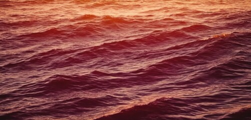  a large body of water with waves in the foreground and a setting sun in the sky in the background.