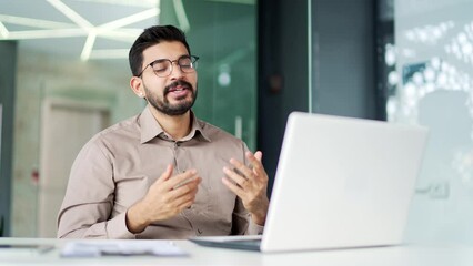 Confident bearded businessman talking on a video call using a laptop sitting at a workplace in business office. A male coach speaks remotely, has a conversation at an online conference or on a webinar