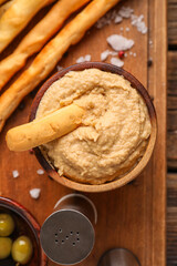 Bowl with tasty hummus and Italian Grissini on wooden background