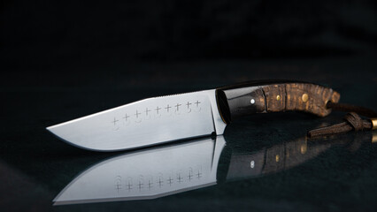 Ein handgeschmiedetes Messer mit einem Griff aus schwarzem Horn auf schwarzem Glas, was das Messer spiegelt