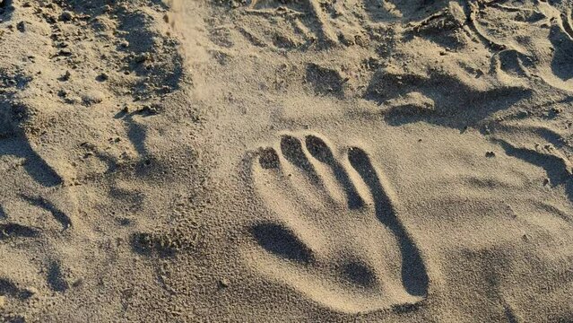 Symbol of passage of time, concept of instability or transformation, handprint on sand gradually disappears under sand falling from above.