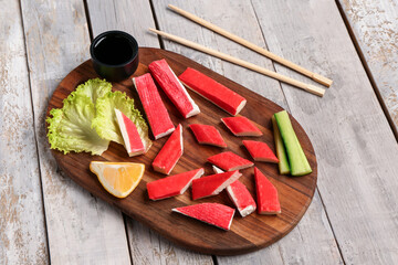 Board with tasty crab sticks and sauce on light wooden background