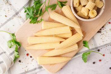 Wooden board with cut and whole canned baby corn cobs on light background