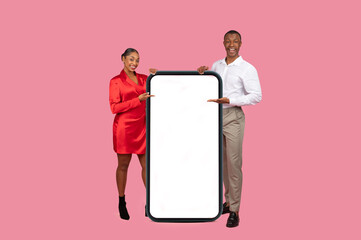 Black couple presenting large smartphone screen, dressed in elegant clothes