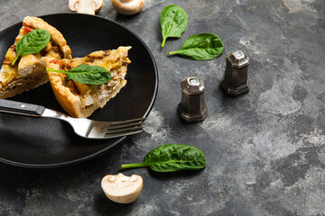 Pieces of mushroom pie with spinach leaves and champignons on black grunge table