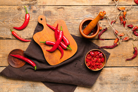 Board of fresh and dry hot chili peppers with mortar on brown wooden background