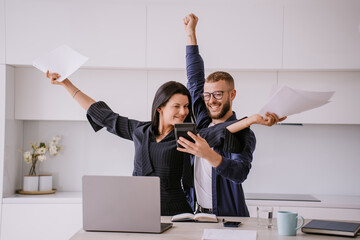 Two professionals celebrate a success with papers and digital tablet in a bright office.