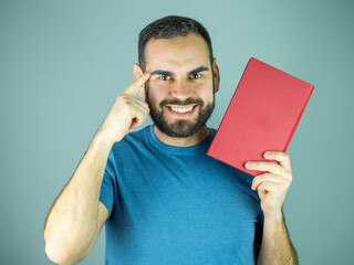 Young man pointing his head while holding a red book Looking at camera