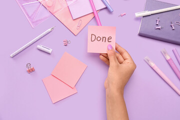 Obraz premium Woman holding sticky note with word DONE and stationery on lilac background
