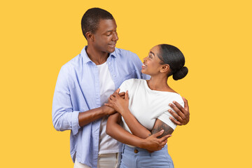 Loving black couple looking at each other, smiling on yellow backdrop