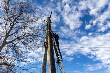 A technician working on a ladder to maintain fiber optic wires attached to electric poles and...