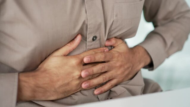 Close up. Male hands holding massaging stomach. Businessman in shirt feels stomach pain sitting at workplace in business office. Sick man suffers from bloating, gastritis poisoning, bloating or spasms