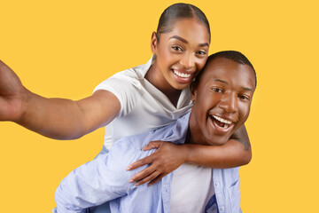 Obraz premium Black couple taking selfie, joyful expressions on yellow background