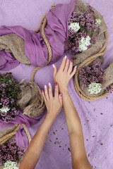 Women's manicured hands and a floral arrangement with burlap on a lilac background.