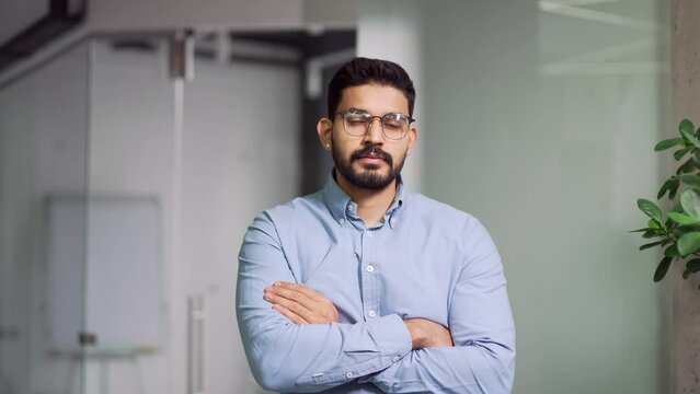 Portrait of a serious bearded businessman in shirt standing with crossed arms in business office. Confident successful boss owner posing looking at camera. Head shot of handsome smiling manager