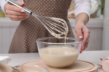 Woman making dough with whisk in bowl at table, closeup