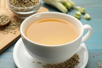 Fennel tea in cup, seeds and fresh vegetable on light blue wooden table, closeup