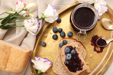 Tray with bread pieces, jar of blueberry jam and flowers on table, closeup