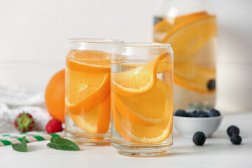 Glasses and bottle of infused water with orange slices on white table