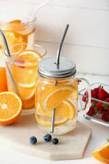 Glasses and mason jar of infused water with orange slices on white table