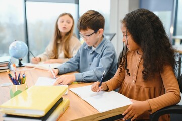 Focused multiracial students kids writing down data into notebook while sitting at table