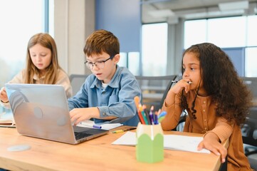 Portrait of smart schoolgirls and schoolboys looking at the laptop in classroom