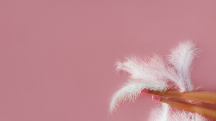 Doll's feet in plastic shoes lying on white feathers on pink background