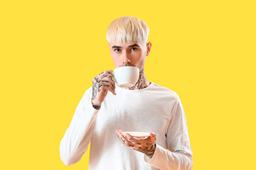 Young tattooed man drinking coffee on yellow background