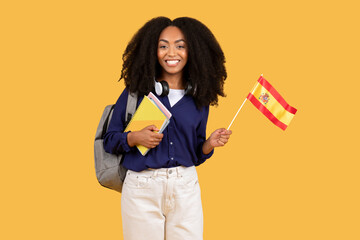Happy black female student with backpack and copybooks, holding Spanish flag, symbolizing language...