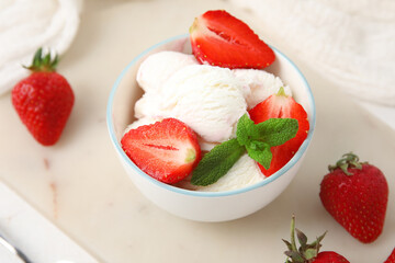 Bowl of vanilla ice cream with strawberries, mint and spoon on white table