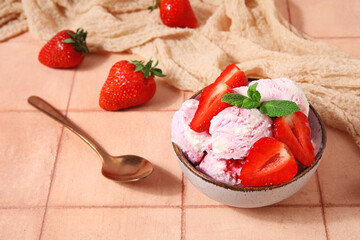 Bowl of strawberry ice cream with berries, mint and spoon on beige tile table