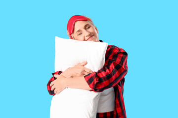 Mature woman in pajamas with pillow on blue background