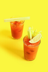 Glasses of bloody mary with celery and lime on yellow background