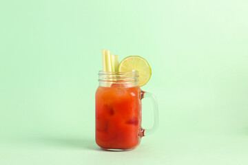 Mason jar of bloody mary with celery and lime on green background