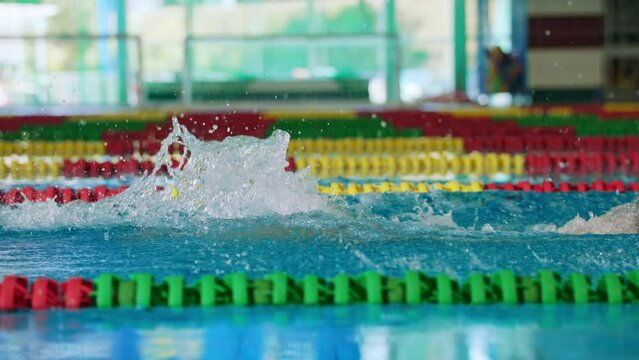 Slow motion of male professional athlete swimming in butterfly style, with both arms moving symmetrically, making water splash, tracking slow motion shot.
