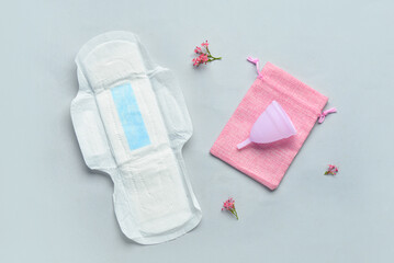 Composition with menstrual pad, cup, bag and flowers on grey background
