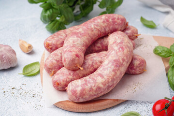 Wooden board with raw homemade sausages on light background