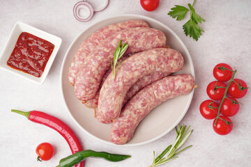 Plate with raw homemade sausages and sauce on light background