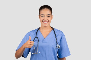 Confident European millennial doctor in blue scrubs giving a thumbs-up