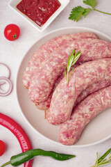Plate with raw homemade sausages on light background