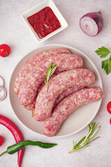 Plate with raw homemade sausages and sauce on light background