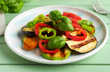 Plate with grilled vegetables and basil on green wooden table