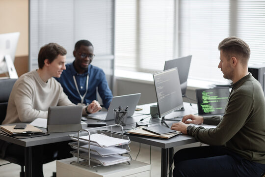 Wide shot of multi-ethnic male IT team working on new cyber security project while sitting at desks of modern company office