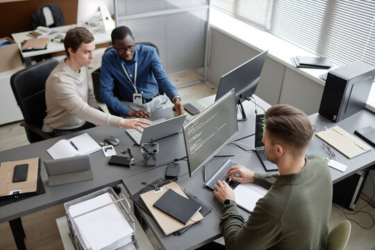 High angle shot of busy IT professionals sitting at office desks while developing cybersecurity protocols during workday in modern IT company
