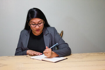 Mujer caucásica con chaqueta gris escribiendo  sentada cerca de la mesa sonriendo