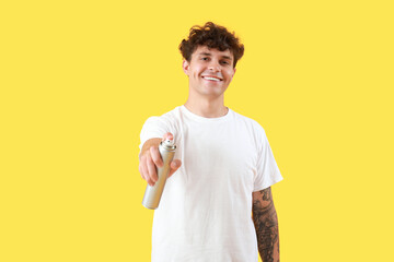 Handsome young man with bottle of hair spray on yellow background