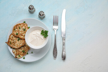 Plate of tasty zucchini fritters with sour cream on light background